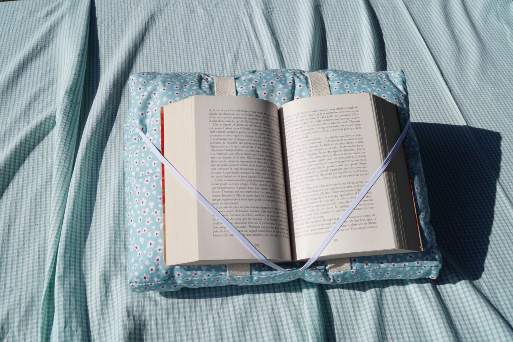 Coussin de lecture - bleu et petites fleurs blanches - le livre est ouvert et les pages maintenues par des élastiques